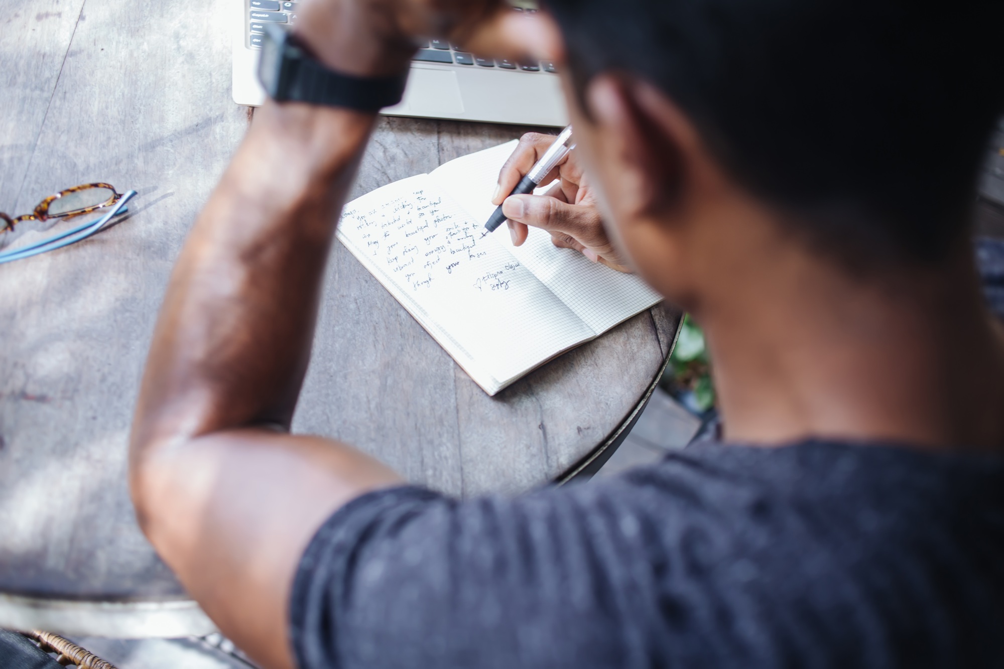 Ethnic newsman sketching notes and using laptop at cafe